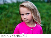 A young girl stands amidst vibrant green grass, wearing a bright pink coat. Her serious expression contrasts with the playful color of her outfit, creating an intriguing visual narrative. Стоковое фото, фотограф Aleksandr Golubev / Фотобанк Лори