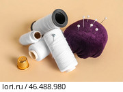 Катушки с нитками, наперсток и игольница с шариковыми штифтами на цветном фоне. Стоковое фото, фотограф Pixel_shot / Фотобанк Лори