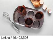 Противень для маффинов с бумажными формами, венчиком и яйцами на светлом фоне. Стоковое фото, фотограф Pixel_shot / Фотобанк Лори