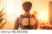Young man wearing posture corrector brace at home during sunset. Стоковое AI-изображение, AI-художник Юрий Поздников / Фотобанк Лори