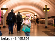 Inside the subway, a cheerful five-year-old girl stands out against the backdrop of busy commuters. Dressed warmly, she radiates joy amid the hustle of the underground. Стоковое фото, фотограф Aleksandr Golubev / Фотобанк Лори