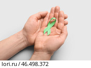 Мужские руки с зеленой лентой на светлом фоне, крупным планом. Концепция митохондриальных заболеваний и рака почки. Стоковое фото, фотограф Pixel_shot / Фотобанк Лори