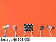 Множество рук с ведром попкорна, кинематографическим хлопком и мегафонами на оранжевом фоне. Стоковое фото, фотограф Pixel_shot / Фотобанк Лори