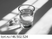 A clear glass of water and several white pills neatly laid out on a light surface. The sunlight coming through the window creates soft shadows and highlights, emphasizing the minimalism and purity of the composition. The atmosphere of the photo conveys a sense of calm, meditativeness, but at the same time hints at the theme of health, self-care or treatment. Стоковое AI-изображение, AI-художник Анна Кривицкая / Фотобанк Лори