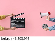 Руки с киношным хлопушкой, катушкой с пленкой и громкоговорителем на розовом фоне. Стоковое фото, фотограф Pixel_shot / Фотобанк Лори