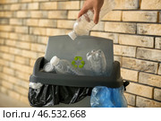 Женщина бросает пластиковую бутылку в мусорное ведро возле кирпичной стены. Стоковое фото, фотограф Pixel_shot / Фотобанк Лори