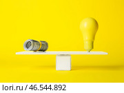 Долларовые банкноты и лампочка на подкидной доске на желтом фоне. Концепция баланса. Стоковое фото, фотограф Pixel_shot / Фотобанк Лори