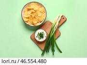 Миска вкусной сметаны с нарезанным луком-пореем и картофельными чипсами на зеленом фоне. Стоковое фото, фотограф Pixel_shot / Фотобанк Лори