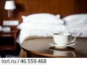 A white cup of hot tea or coffee on a wooden table in the interior of a hotel room. The concept of drinks and comfortable hotel accommodation. Стоковое фото, фотограф Photojuli / Фотобанк Лори