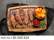 Деревянная доска для шашлыка с вкусным люля-кебабом, соусом и овощами-гриль на черном фоне. Стоковое фото, фотограф Pixel_shot / Фотобанк Лори