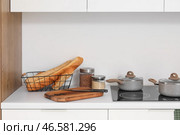 Белые кухонные столешницы с разделочной доской, электрической плитой, кастрюлями и кухонными принадлежностями. Стоковое фото, фотограф Pixel_shot / Фотобанк Лори