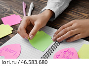 Женщина прикрепляет записку к блокноту за деревянным столом. Стоковое фото, фотограф Pixel_shot / Фотобанк Лори