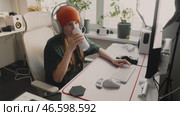 Enthusiastic female gamer in cozy, well lit gaming space drinks soda and interacts with friends online. Focused on screen, she enjoys both game and social connection in her stylish setup. Стоковое видео, видеограф Енваев Андрей / Фотобанк Лори