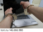 Наручники на руках преступника, занимавшегося мошенничеством в сети Интернет, и ноутбук. Стоковое фото, фотограф Сергей Булкин/NEWS.ru / ТАСС / Фотобанк Лори