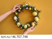 Женщина вешает пасхальный венок на желтую стену. Стоковое фото, фотограф Pixel_shot / Фотобанк Лори