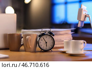 Будильник с бумагами и чашками кофе на столе в офисе ночью, крупный план. Концепция дедлайна. Стоковое фото, фотограф Pixel_shot / Фотобанк Лори