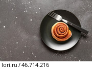 Тарелка с вкусной булочкой с корицей на черном фоне. Стоковое фото, фотограф Pixel_shot / Фотобанк Лори