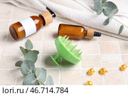 Силиконовая массажная щетка для головы с бутылками косметических продуктов, ванночной губкой и эвкалиптом на бежевом плиточном фоне. Стоковое фото, фотограф Pixel_shot / Фотобанк Лори