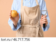 Женщина держит сырой картофель и овощечистку на коричневом фоне. Стоковое фото, фотограф Pixel_shot / Фотобанк Лори