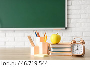 Яблоко, книги, будильник и канцелярские принадлежности на учительском столе в классе. Концепция возвращения в школу. Стоковое фото, фотограф Pixel_shot / Фотобанк Лори
