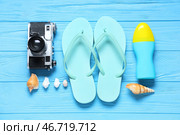 Стильные шлепанцы, ракушки, фотоаппарат и бутылка с солнцезащитным кремом на фоне синего деревянного настила. Стоковое фото, фотограф Pixel_shot / Фотобанк Лори