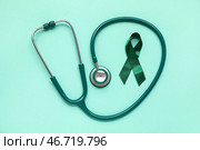 Атласная зеленая лента и стетоскоп на бирюзовом фоне. Национальный месяц осведомленности о церебральном параличе. Стоковое фото, фотограф Pixel_shot / Фотобанк Лори