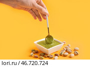 Женская рука с ложкой и миска с вкусной фисташковой пастой на жёлтом фоне. Стоковое фото, фотограф Pixel_shot / Фотобанк Лори