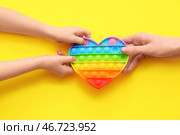 Детские и женские руки с игрушкой-антистресс pop it на желтом фоне, крупный план. Стоковое фото, фотограф Pixel_shot / Фотобанк Лори