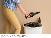 Женщина бросает бутылку в контейнер для стекла у бежевой стены. Концепция переработки. Стоковое фото, фотограф Pixel_shot / Фотобанк Лори
