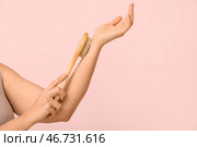 Молодая женщина массирует руку массажной щеткой для тела на розовом фоне. Стоковое фото, фотограф Pixel_shot / Фотобанк Лори