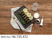 Разделочная доска с вкусными долмой (фаршированными виноградными листьями), сметаной, специями и стаканом воды на деревянном фоне. Стоковое фото, фотограф Pixel_shot / Фотобанк Лори