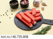 Чёрная доска с вкусными крабовыми палочками и различными специями на жёлтом фоне. Стоковое фото, фотограф Pixel_shot / Фотобанк Лори