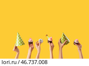 Множество женских рук с праздничными капкейками, дудочками и праздничными колпаками на жёлтом фоне. Стоковое фото, фотограф Pixel_shot / Фотобанк Лори