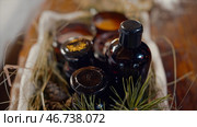 Aromatherapy table setting with perfumed candles, oil bottle and coniferous twig with cones creating mood. Стоковое фото, фотограф David Kashakhi / Фотобанк Лори
