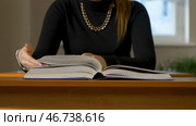 Woman sitting at the table leafing through the book. Стоковое фото, фотограф David Kashakhi / Фотобанк Лори