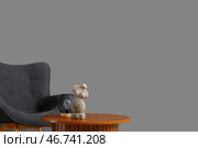 Уютное кресло и деревянный журнальный столик с женской фигуркой возле серой стены. Стоковое фото, фотограф Pixel_shot / Фотобанк Лори