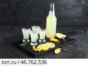 Доска с налитыми рюмками и бутылкой вкусного лимончелло на черном фоне. Стоковое фото, фотограф Pixel_shot / Фотобанк Лори