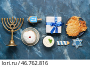 Композиция к Хануке с менаорой, пончиками, подарочным ящиком и картофельными оладьями на темно-синем столе. Стоковое фото, фотограф Pixel_shot / Фотобанк Лори