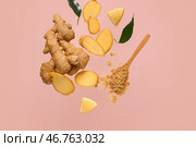 Летающие ломтики свежего корня имбиря и деревянная ложка с сухим порошком на розовом фоне. Стоковое фото, фотограф Pixel_shot / Фотобанк Лори