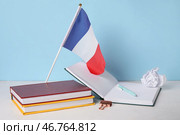 Флаг Франции с книгами и скомканной бумагой на столе возле синей стены. Стоковое фото, фотограф Pixel_shot / Фотобанк Лори