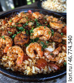 A delicious dish of shrimp, fried to a golden crisp, served with rice, tomatoes and spices. The entire dish is sprinkled with fresh herbs, probably parsley or green onions. The delicious texture of the shrimp with a crispy crust and the rich colors create a sense of spice and flavor. The dish is served in a deep cast iron skillet, and in the background is an additional side dish, presumably macaroni or cheese spread. Стоковое AI-изображение, AI-художник Анна Кривицкая / Фотобанк Лори