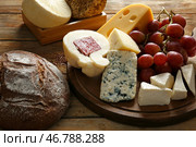 Деревянная доска с ассортиментом вкусных сыров и хлеба на столе. Стоковое фото, фотограф Pixel_shot / Фотобанк Лори