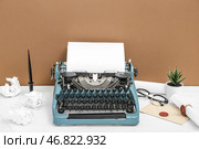 Винтажная печатная машинка, очки, подставка для ручек, конверт и свитки с печатью из воска на белом столе около коричневой стены. Стоковое фото, фотограф Pixel_shot / Фотобанк Лори