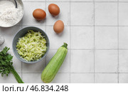 Чашки с тертыми кабачками, мукой и яйцами для приготовления оладий на белом плиточном фоне. Стоковое фото, фотограф Pixel_shot / Фотобанк Лори