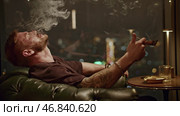 Brutal man smokes cigar. Media. Attractive man with beard smokes cigar coolly. Cinematic cigar smoking with brutal man in restaurant. Стоковое фото, фотограф Данил Руденко / Фотобанк Лори