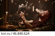 Brutal man smokes cigar. Media. Attractive man with beard smokes cigar coolly. Cinematic cigar smoking with brutal man in restaurant. Стоковое фото, фотограф Данил Руденко / Фотобанк Лори