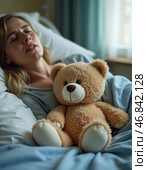 In a cozy hospital room, a woman lays in bed, her eyes shut, a teddy bear nestled beside her. Despite hardships, she clings to hope for a brighter tomorrow. Стоковое AI-изображение, AI-художник Юлия Петровская / Фотобанк Лори