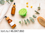 Силиконовая массажная щетка для головы с бутылками косметических продуктов, ванночной губкой и эвкалиптом на бежевом плиточном фоне. Стоковое фото, фотограф Pixel_shot / Фотобанк Лори