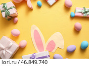 Рамка из бумажных зайчих ушей, пасхальных яиц и подарочных коробок на желтом фоне. Стоковое фото, фотограф Pixel_shot / Фотобанк Лори