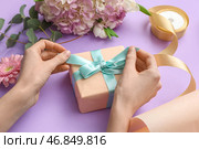 Женские руки с подарочной коробкой, оберточной бумагой и красивыми цветами на фиолетовом фоне. Международный женский день. Стоковое фото, фотограф Pixel_shot / Фотобанк Лори